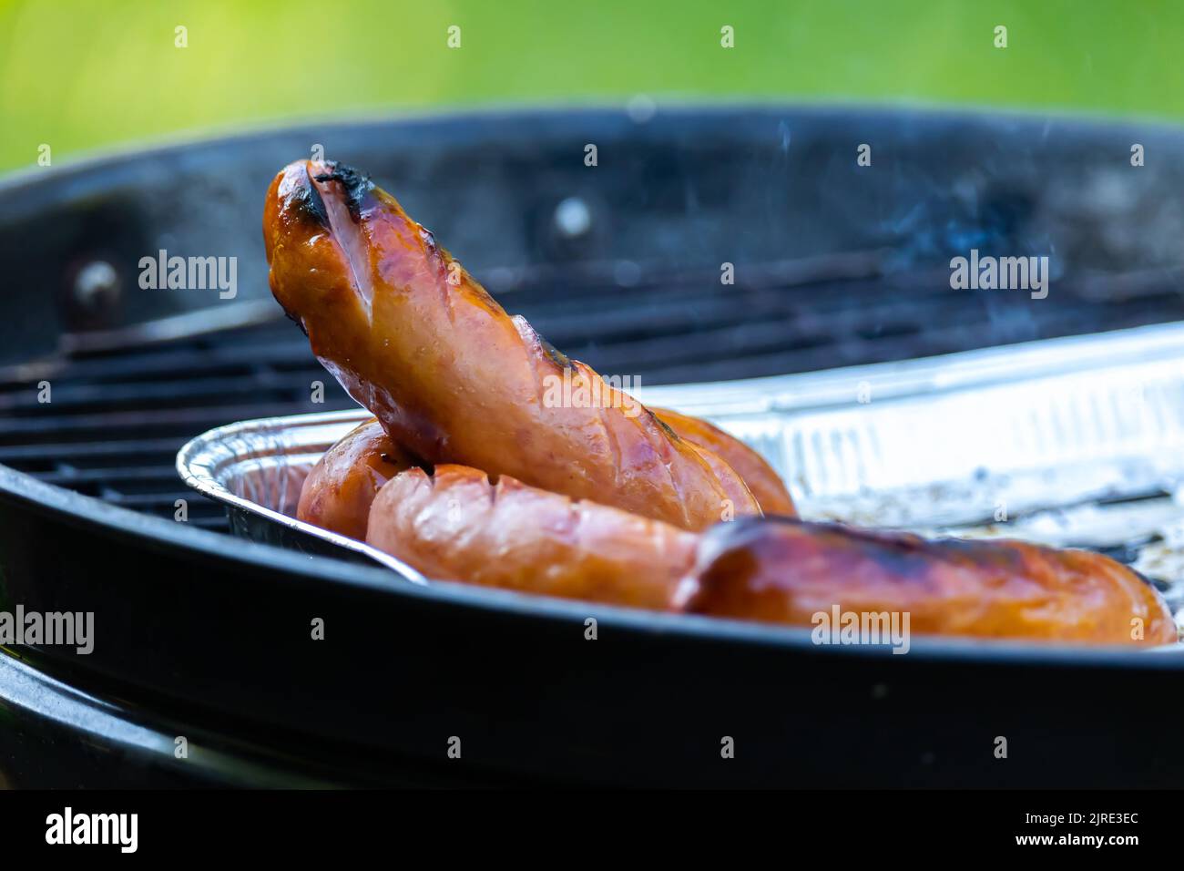 Grilled sausage sizzling on an aluminum tray on the garden grill Stock