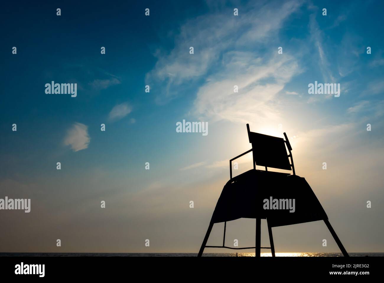 The dark outlines of a tall lifeguard observation chair on the beach. Photo taken against the sun on a sunny afternoon Stock Photo