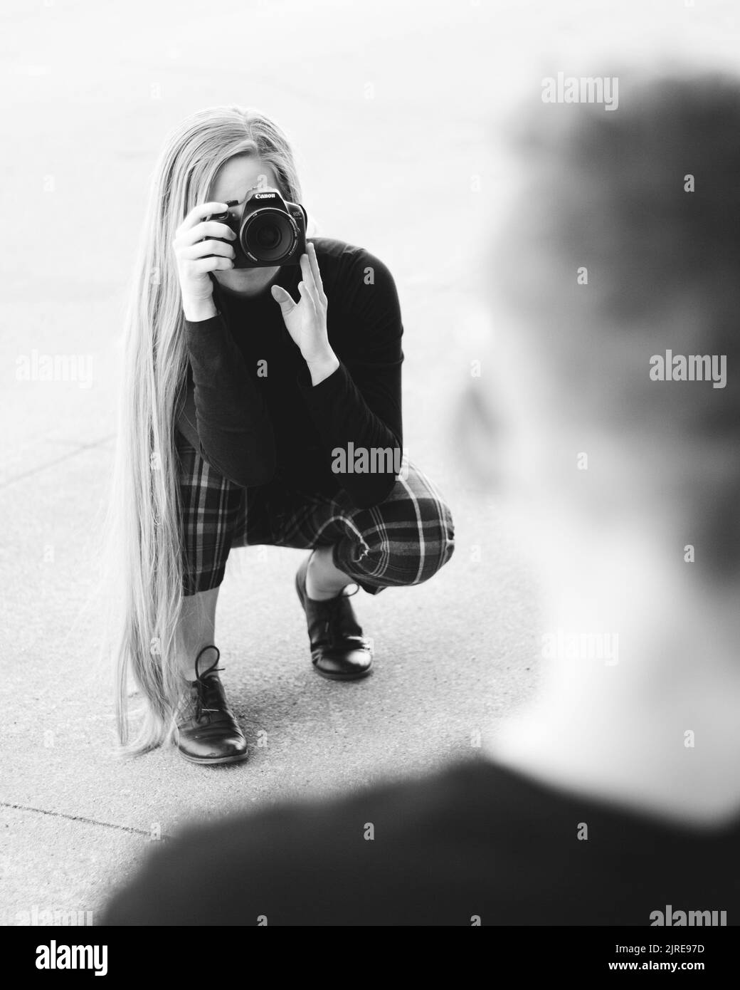 A vertical grayscale shot of a female with long hair taking photos with a professional camera Stock Photo