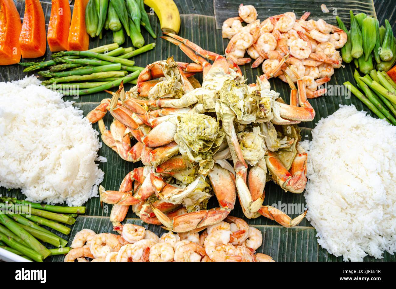 Boodle fight is a Filipino social meal or buffet eaten using hands seen here including crab, prawns, okra, asparagus and boiled rice. Stock Photo