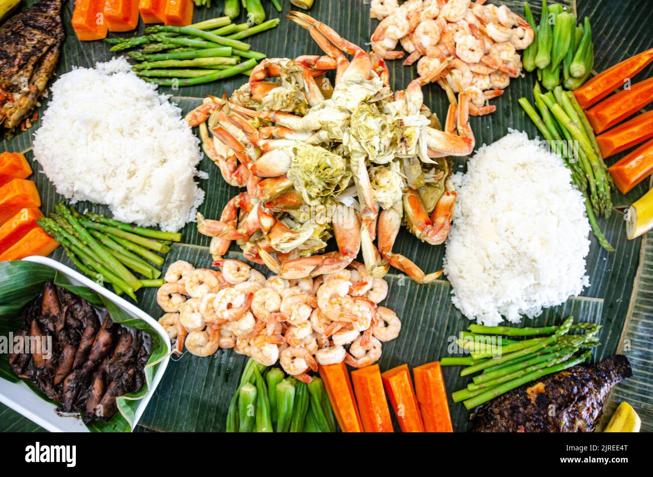 Boodle fight is a Filipino social meal or buffet eaten using hands seen here including crab, prawns, okra, asparagus and boiled rice. Stock Photo