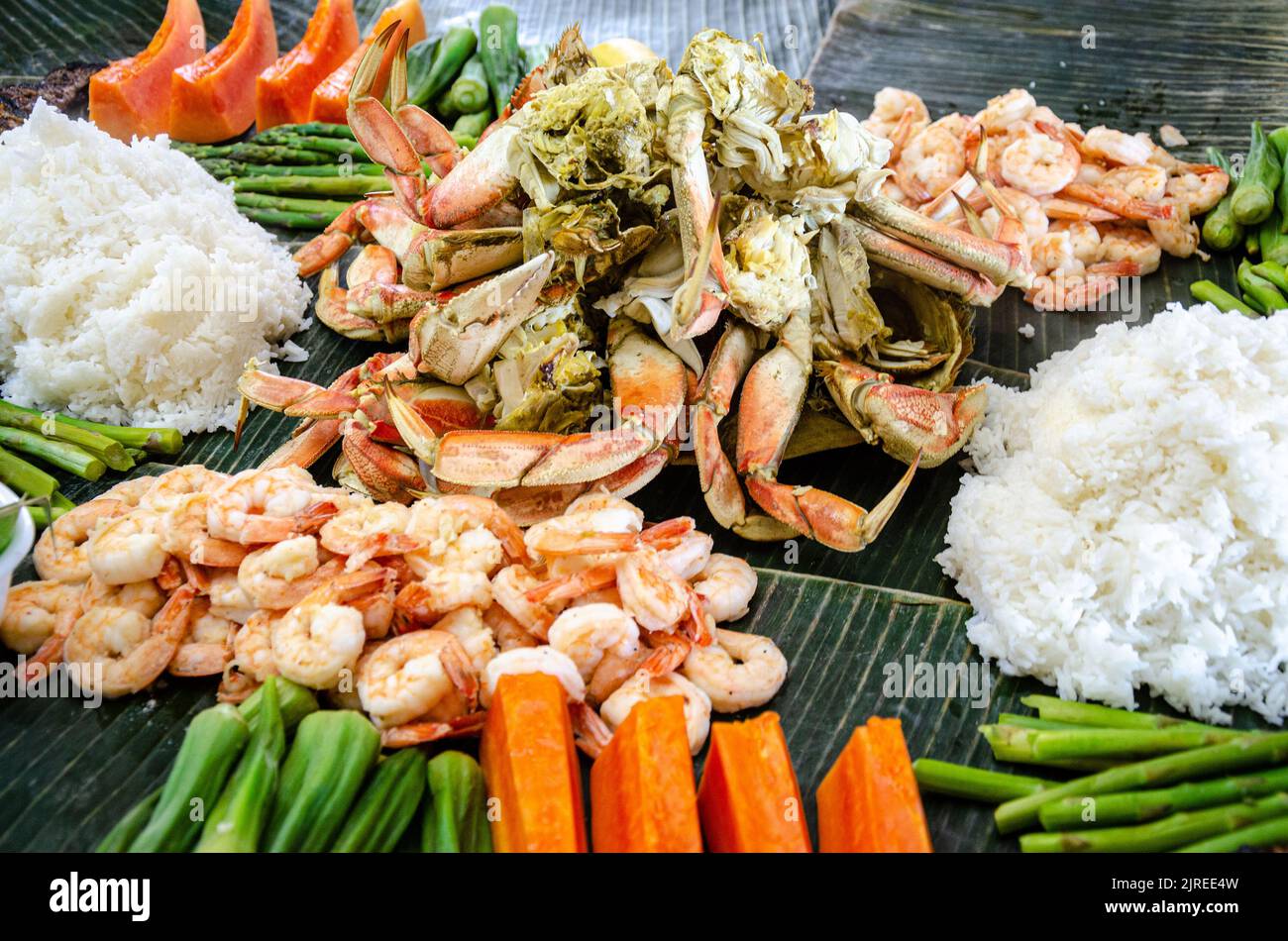 Boodle fight is a Filipino social meal or buffet eaten using hands seen here including crab, prawns, okra, asparagus and boiled rice. Stock Photo