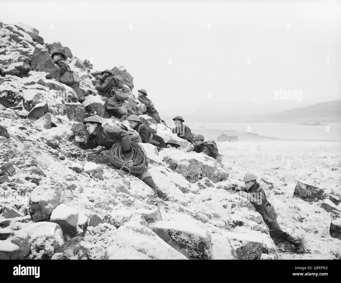 Sailors carrying cable, telephone wires and explosives up a hillside during demolition training training at Hvalfjord in Iceland, 1942. On a snow covered hillside ratings are covering their comrades as they carry cable, telephone wires and explosives to a selected objective during training at Hvalfjord, Iceland. These sailors are undergoing training for demolition work, wherein they are shown how to prepare charges and detonators for the destruction of enemy property and defences, as they would in a landing in enemy occupied country. The men are led by specially trained officers who teach them Stock Photo