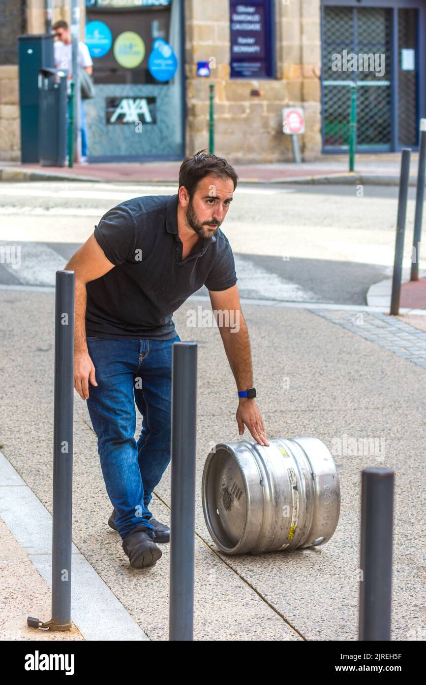 Delivery man rolling metal keg of beer along street - Limoges, Haute-Vienne (87), France. Stock Photo
