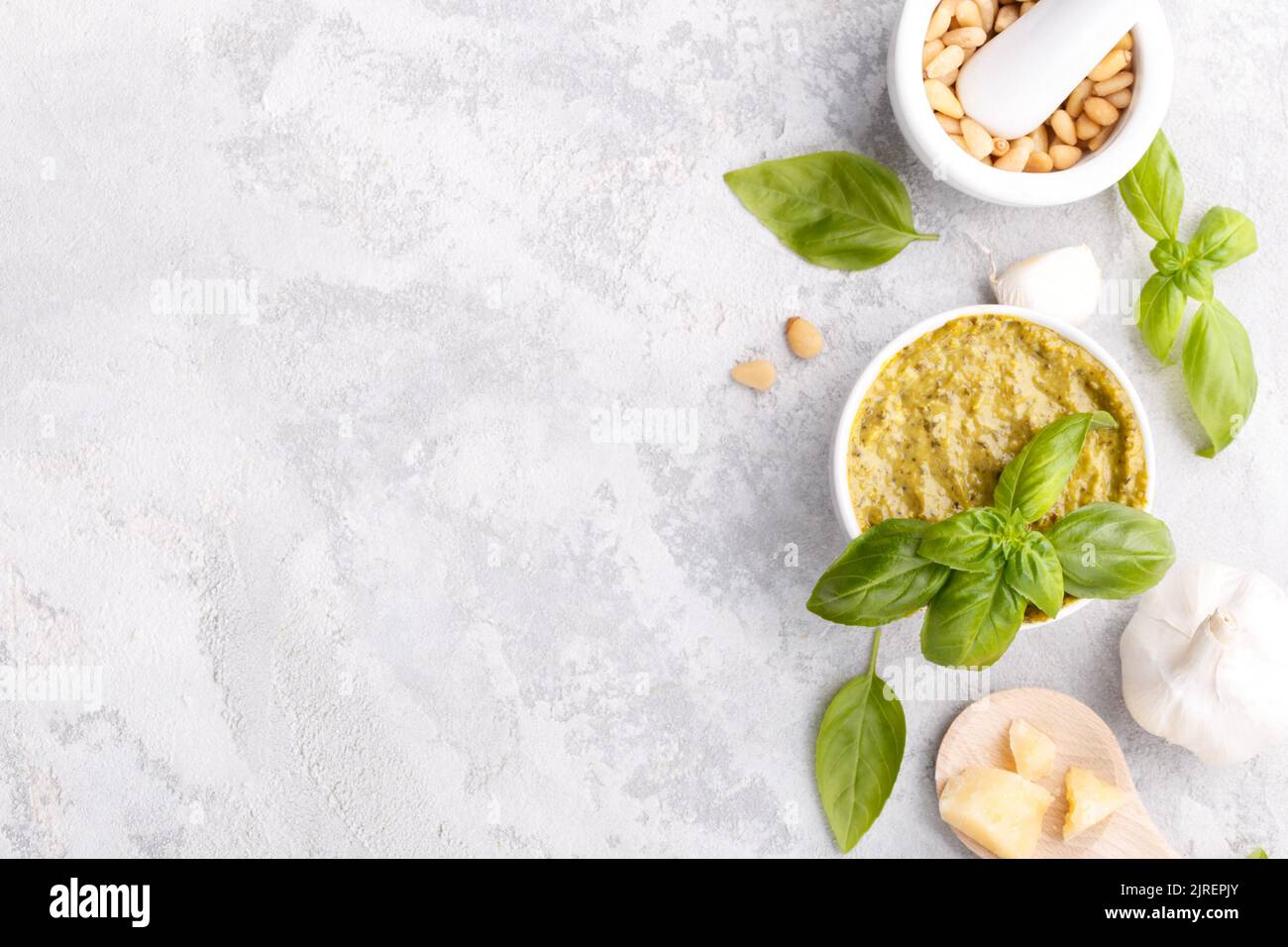 Pesto sauce and ingredients, black cheese board, basil, garlic, pine nuts, olive oil on grey stone background with copy space Stock Photo
