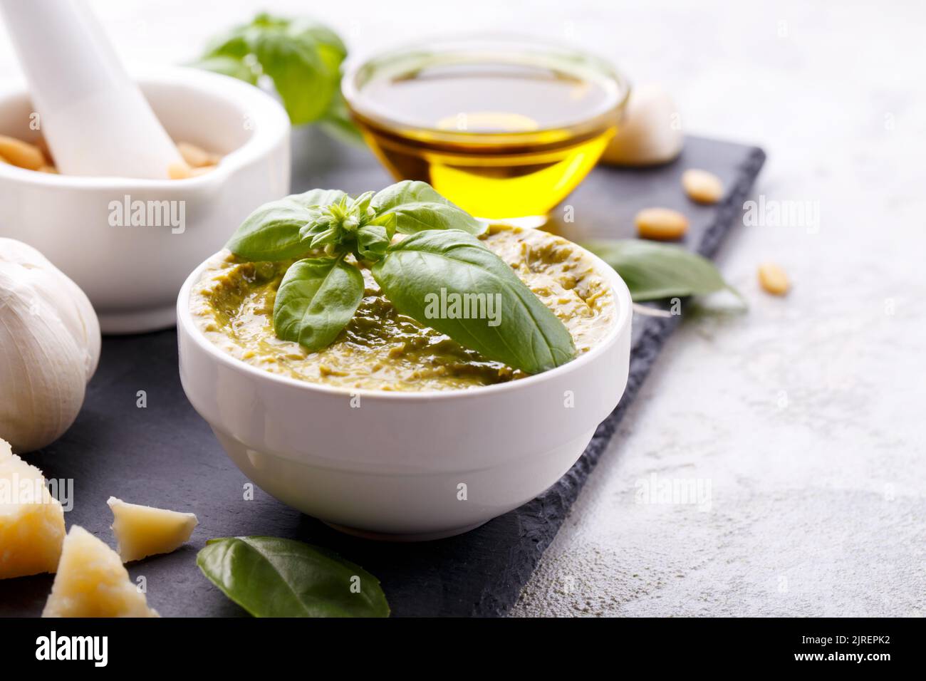 Pesto sauce and ingredients, black cheese board, basil, garlic, pine nuts, olive oil on grey stone background with copy space Stock Photo