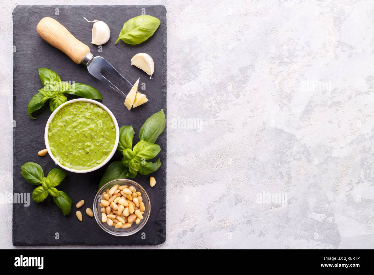 Pesto sauce and ingredients, cheese, basil, garlic, pine nuts, olive oil on black cheese board and grey stone background with copy space Stock Photo