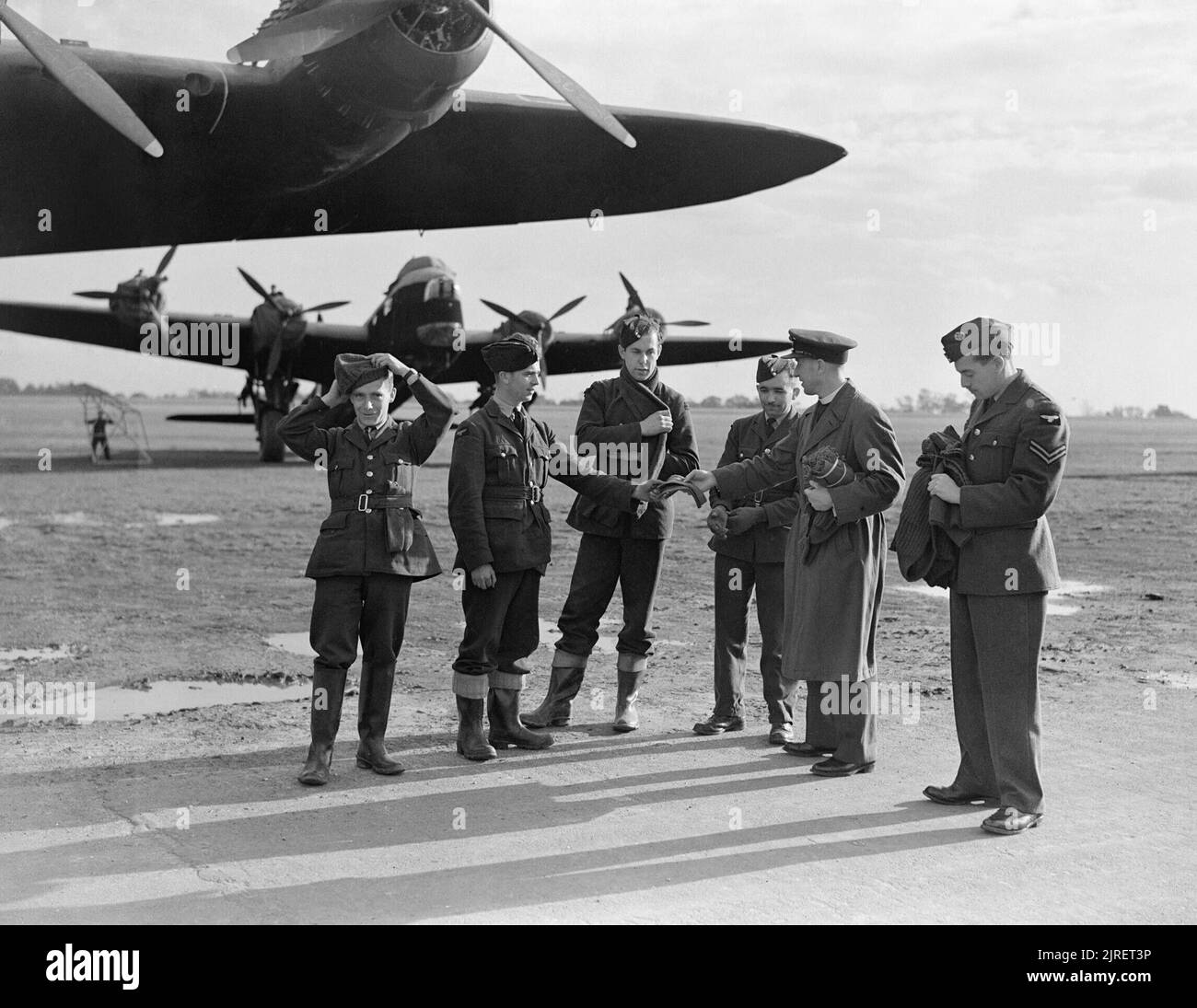 Royal Air Force 1939-1945- Bomber Command Squadron Leader The Reverend E T Killick (second from right), Station Chaplain at RAF Oakington, hands out 'winter warmers' from the RAF Comforts Fund to ground crew on a crisp autumnal morning, 24 October 1942. Two No. 7 Squadron Stirlings are in the background. Stock Photo
