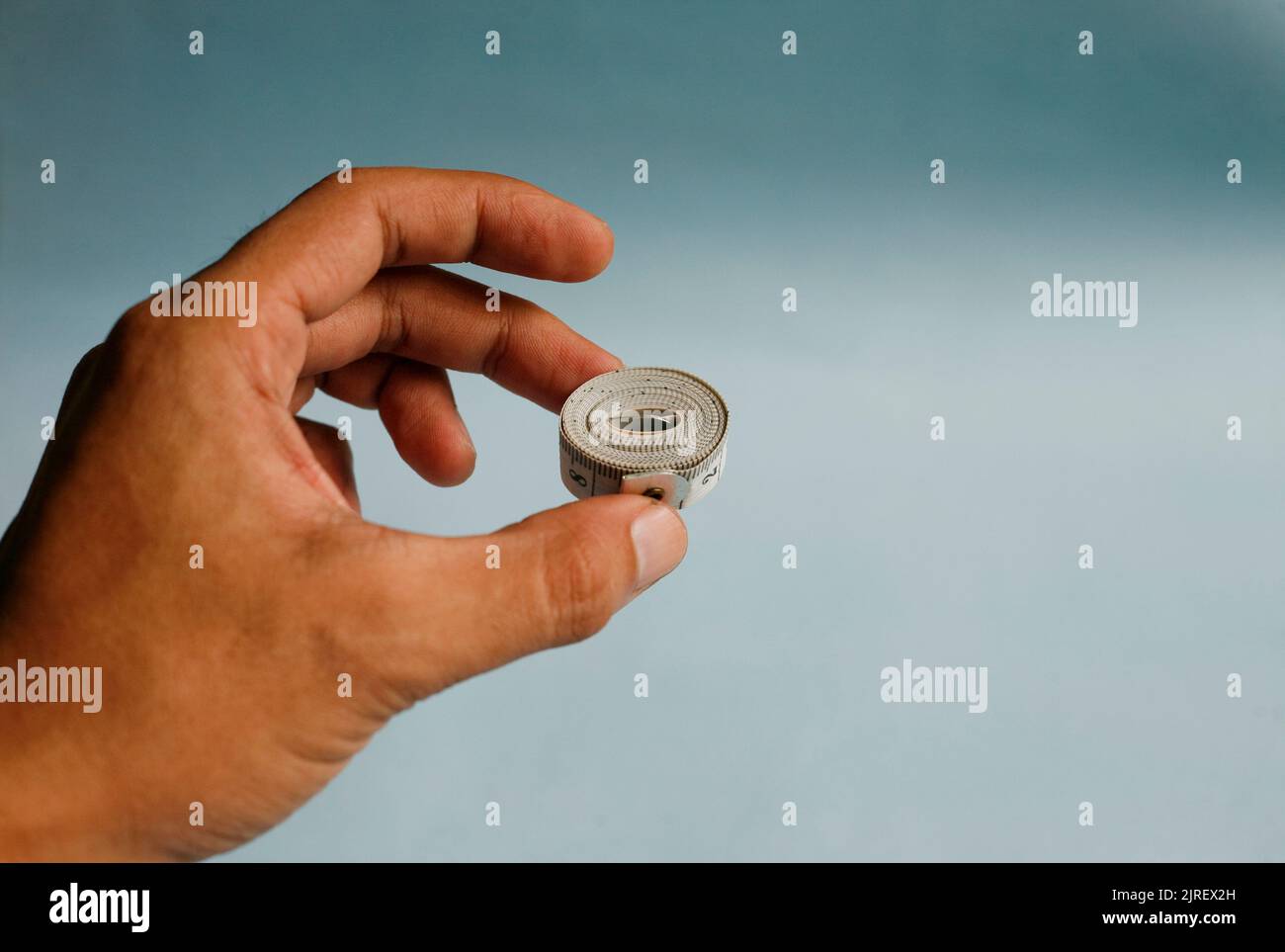 Close up hand holding measuring tape isolated on blue background Stock Photo