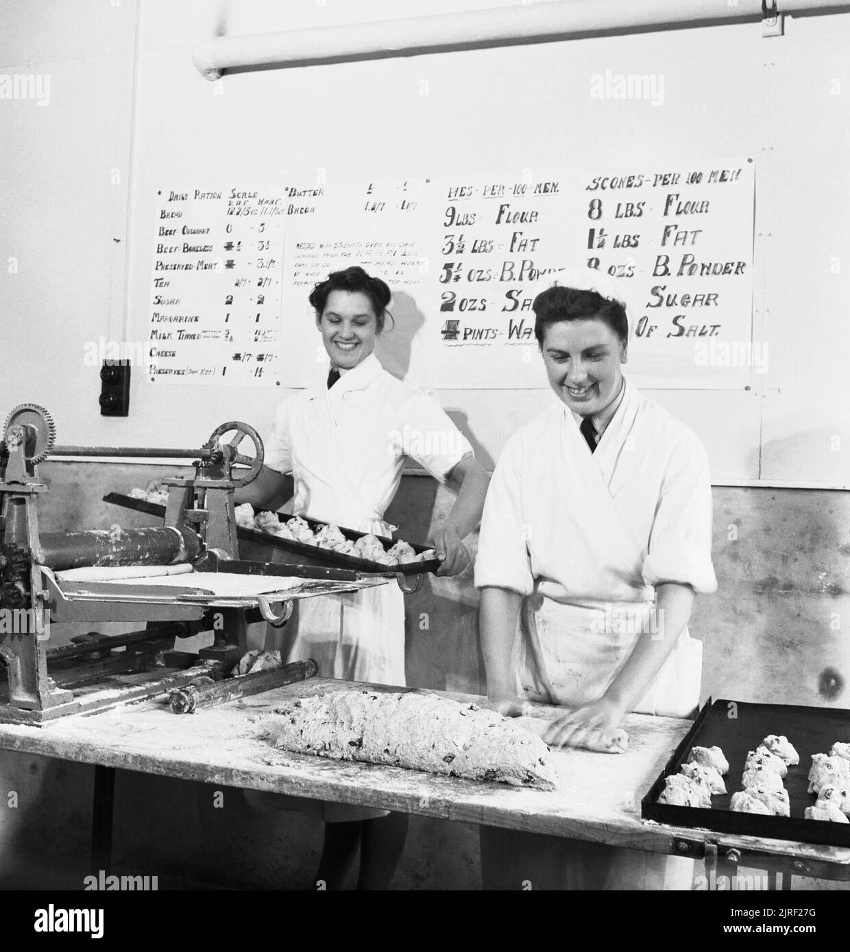 Women's Auxiliary Air Force (WAAF) cooks at work at an RAF station, September 1940. The Women's Auxiliary Air Force (WAAF): Two WAAF cooks at work at a Royal Air Force aerodrome. Pictures behind them are notices bearing recipes for a ?Hundred Pies? and a ?Hundred Scones?. Stock Photo