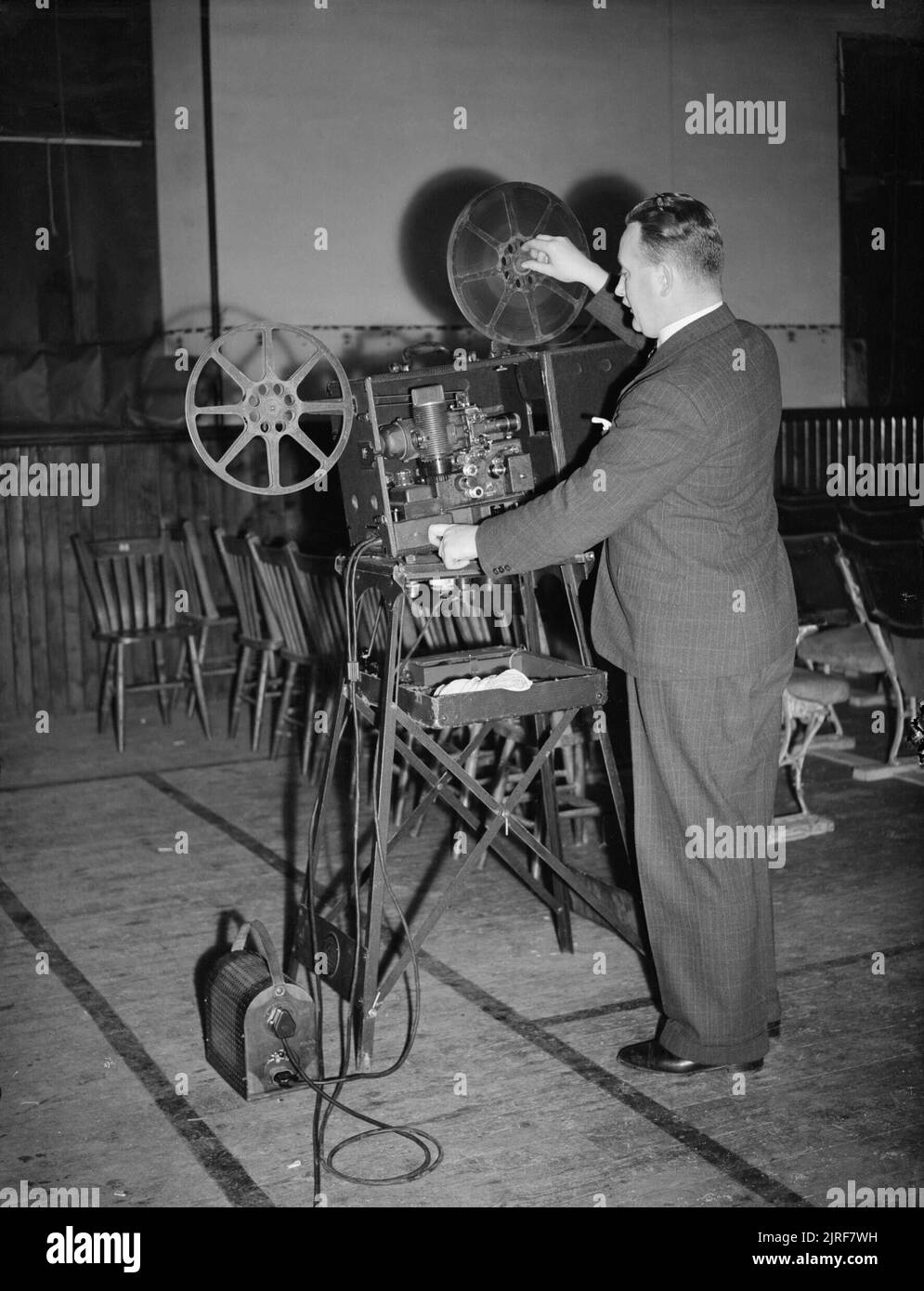 Film Show at Highest Village in the Highlands- Ministry of Information Film Screening, Tomintoul, Banffshire, Scotland, UK, 1943 Ministry of Information Film Operator John Macdougall sets up his Bell and Howell film projector in the Memorial Hall, Tomintoul. The hall is being converted into a cinema for the evening, and just visible are the rows of chairs which have been set up to accommodate the audience. The film is due to begin at 8pm. Stock Photo