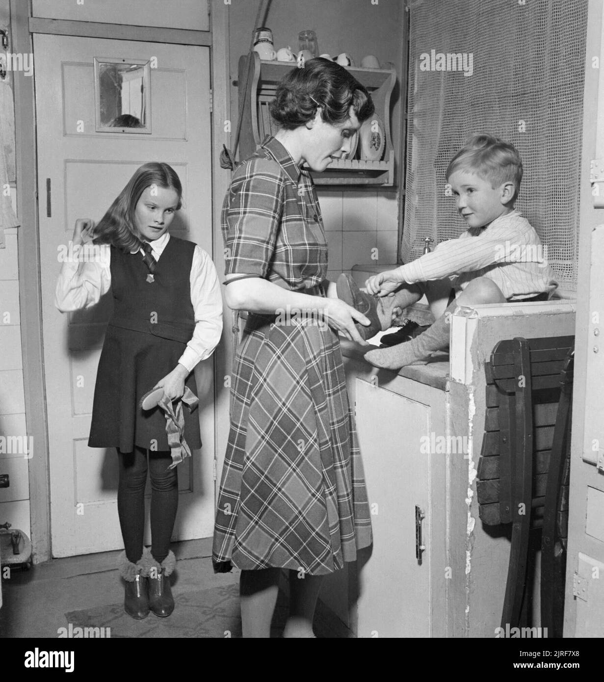 Fireman's Family- Everyday Life in Wartime London, 1942 Mrs Hilda Chillingworth helps her 5 year old son Jeremy put his shoes on, whilst her 8 year old daughter brushes her hair, in the kitchen of their suburban London home. It is eight o'clock in the morning and they are getting ready for school. Although they are not Catholics, they attend the local convent school. Hilda's husband Sydney is in the National Fire Service, and is still at the station, having been on night duty. Stock Photo