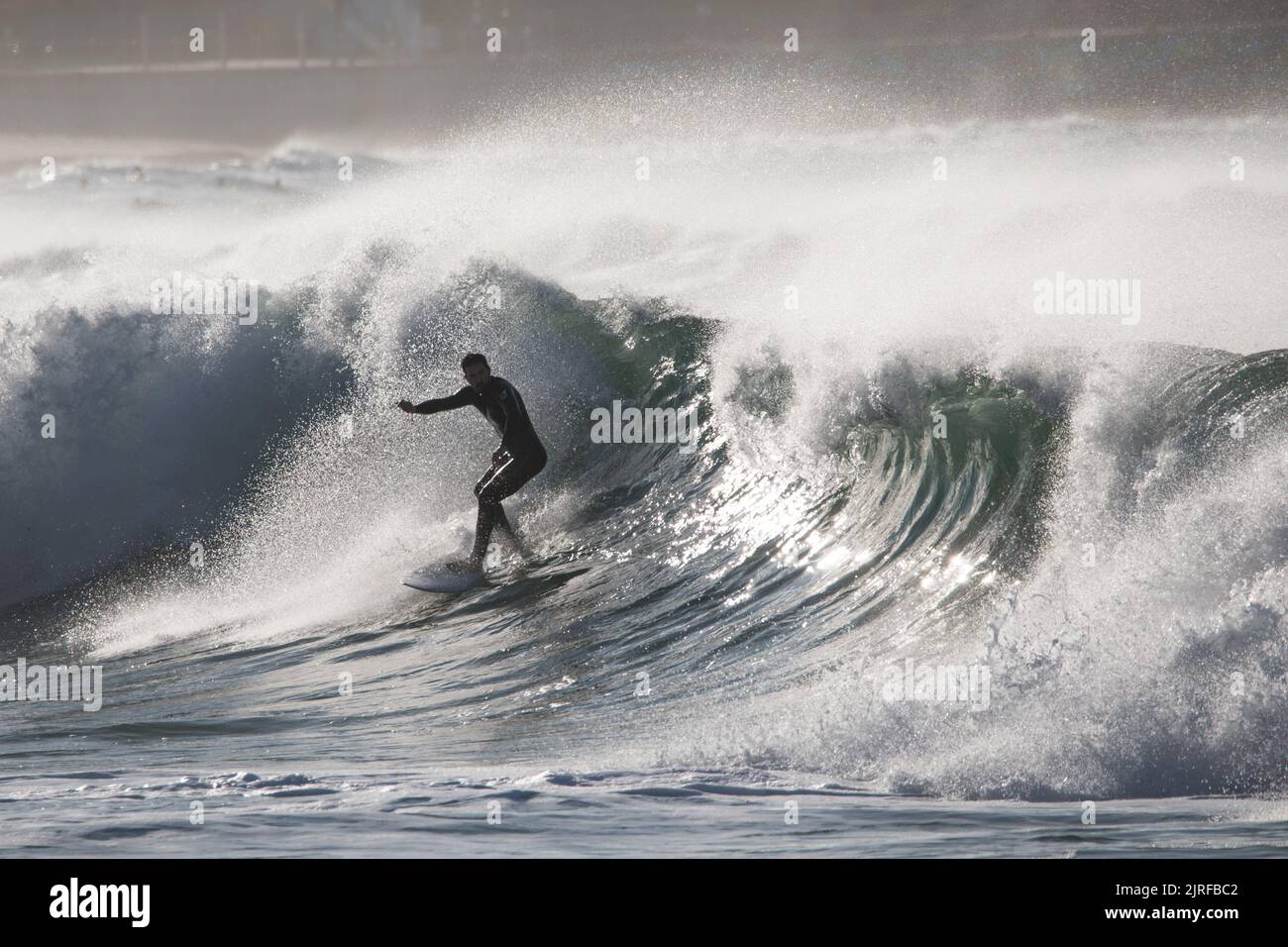 A slim male surfing on foamy high waves splashing in the sea Stock Photo