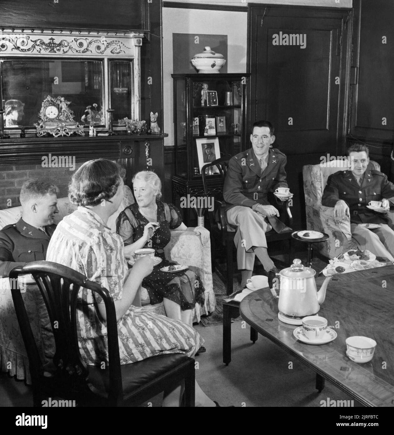 American officers take tea in a house in Winchester, Hampshire during 1944. Lieutenant Loren Bacon (from Eugen, Oregon), Lieutenant Chas Raymond (from New York) and Lieutenant J T Crane (from Chicago) take tea in the home of Mrs A D Weller (left) in Winchester, Hampshire. Stock Photo