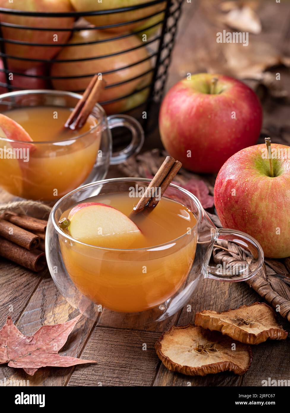 Cup of apple cider with cinnamon stick and sliced apple on a wooden table with fresh apples in background Stock Photo