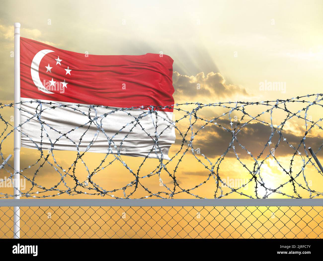 Flagpole with the flag of Singapore against the sky and behind a fence with barbed wire. The concept of protecting the borders of territories. Stock Photo