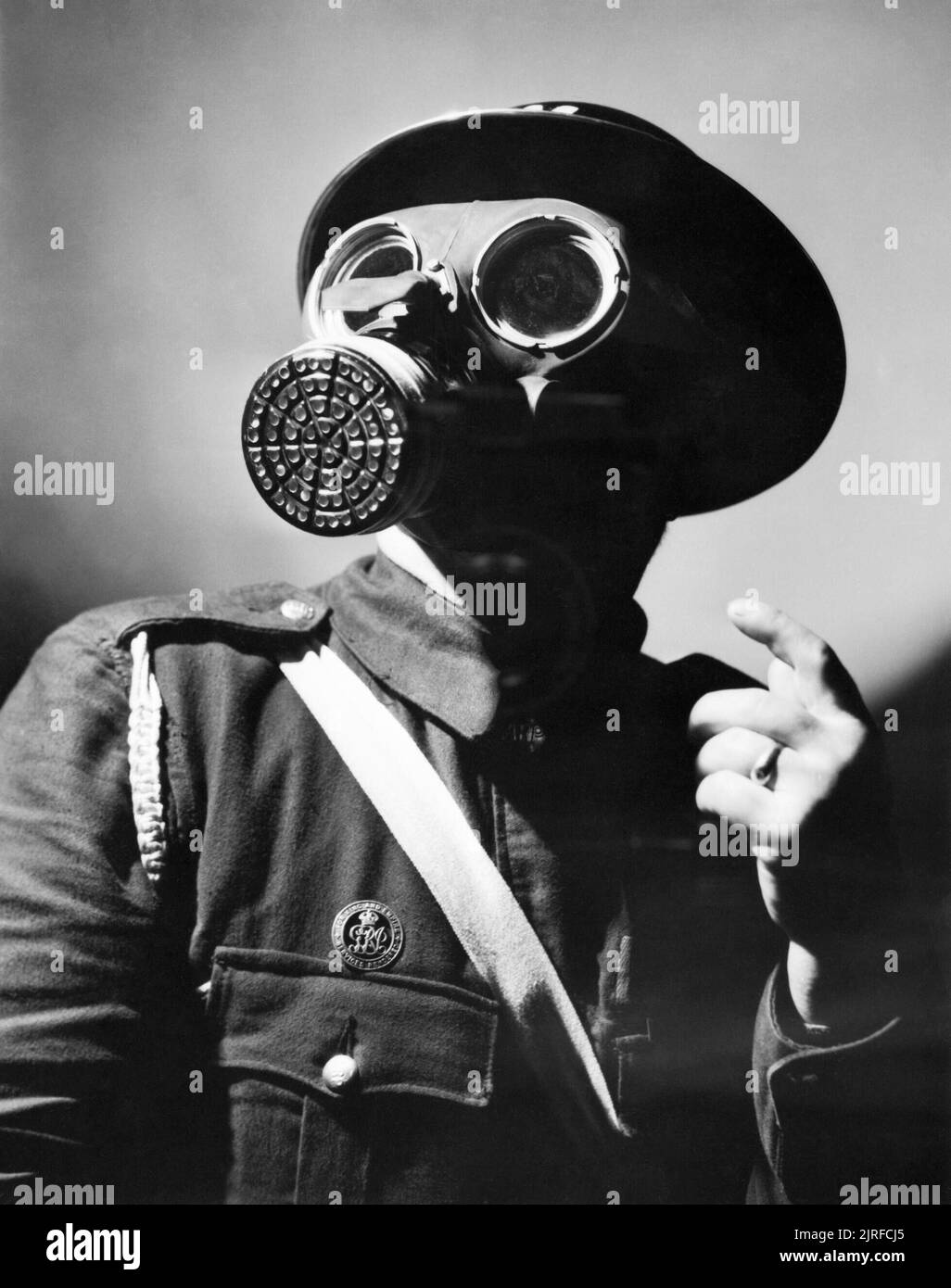 An Air Raid Warden wearing his steel helmet and duty gas mask during the Second World War. A head and shoulders portrait of an Air Raid Warden wearing his steel helmet and duty gas mask. The warden also wears a white sash, probably to make him more visible in the blackout. Stock Photo