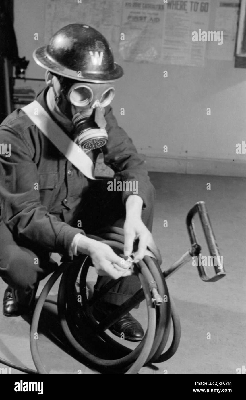 An ARP Warden wearing a gas mask tidies the hose of his stirrup pump at an ARP post in Britain during the Second World War. An ARP Warden wears a gas mask as he crouches down to tie the hose of his stirrup pump into a neat loop at his ARP post, somewhere in Britain. Stock Photo