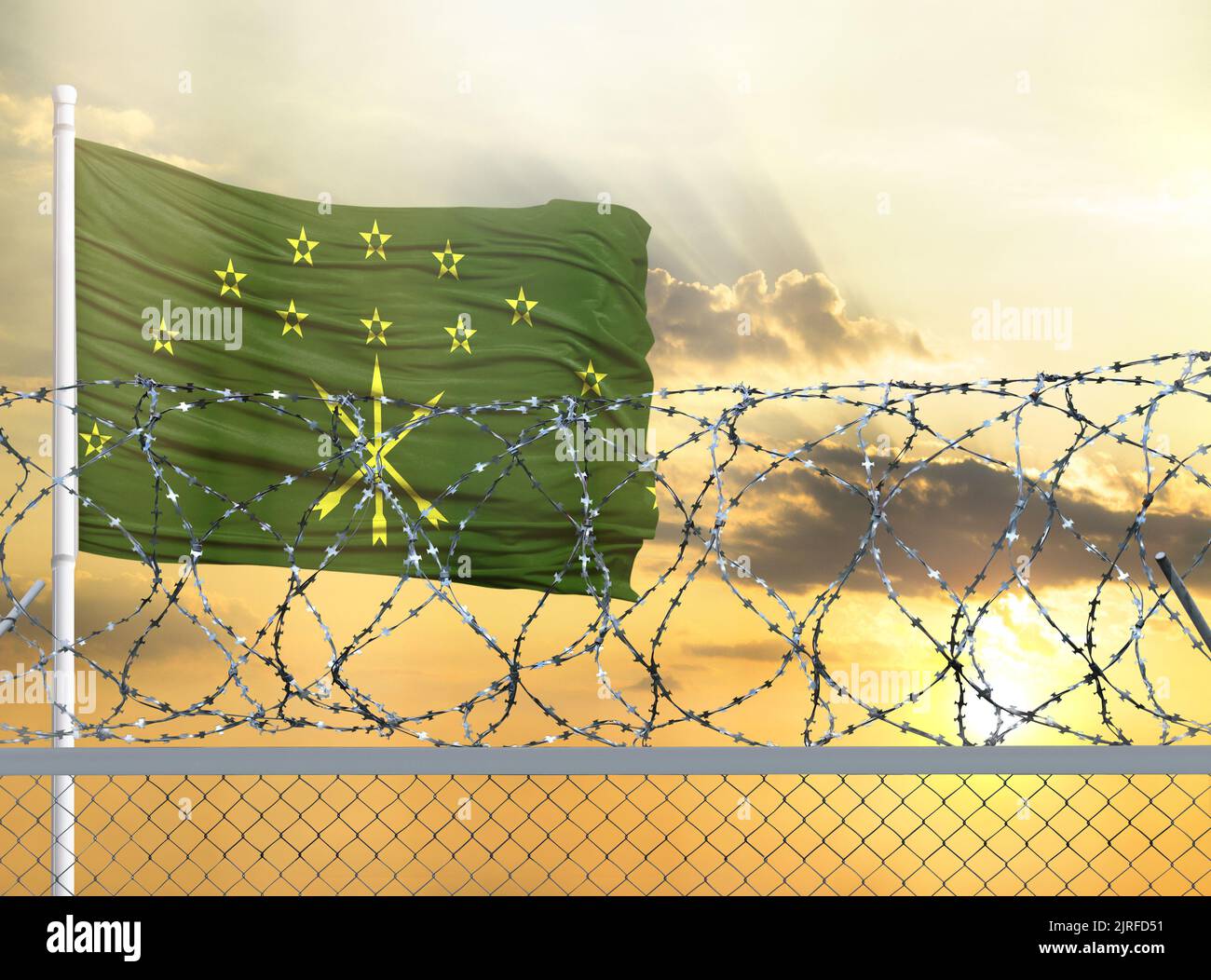 Flagpole with the flag of Adygea against the sky and behind a fence with barbed wire. The concept of protecting the borders of territories. Stock Photo