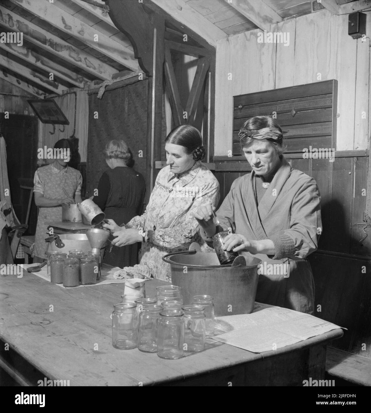 Women's Institute members bottle jam in the Peace Hall at Rowney Green, Worcestershire, 1943. Women's Institute members Mrs Randall (left foreground) and Mrs Dodd (right foreground) bottle jam in the Peace Hall (an army hut converted into a village hall) at Rowney Green, Worcestershire. The fruit was provided by people in the village, from their own gardens, and the sugar came from the government. According to the original caption, this centre has made nearly a ton and three-quarters of jam in the three seasons since the scheme began. Mrs Randall is the centre organiser. Stock Photo