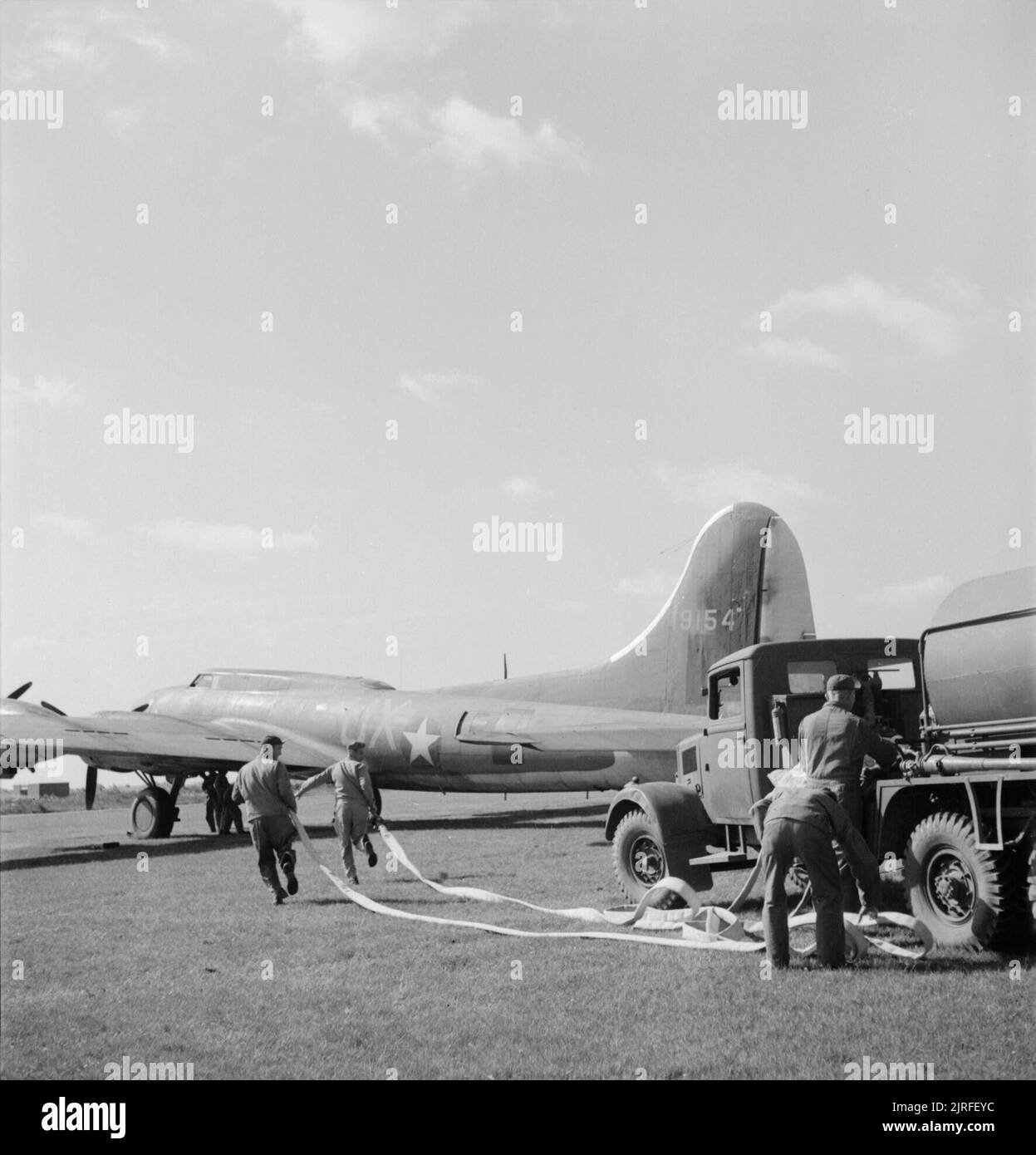 British Equipment at An American Airfield- Anglo-american Co-operation in Wartime Britain, 1943 The crash tender team at an American airfield somewhere in Britain run with their hoses to a B17 Flying Fortress during a drill. The crash tenders are British-made and are posted with ambulances around the airfield when aircraft are due to land in order to provide a quick response to any emergency which may occur. The aircraft features the letters UX, indicating that it is an aircraft of 407 Squadron, 92nd Bombardment Group. Stock Photo