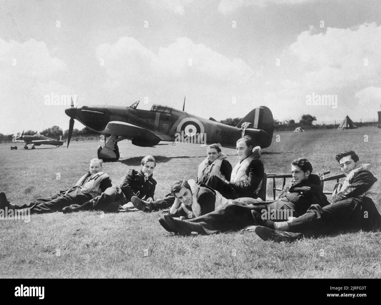 The Battle of Britain Pilots of 'B' Flight, No. 32 Squadron relax on the grass at Hawkinge in front of Hurricane Mk I P3522, GZ-V. From left to right: Pilot Officer R F Smythe; Pilot Officer K R Gillman; Pilot Officer J E Procter; Flight Lieutenant P M Brothers; Pilot Officer D H Grice; Pilot Officer P M Gardner and Pilot Officer A F Eckford. All survived the war except Keith Gillman who was posted missing 25 August 1940. Stock Photo