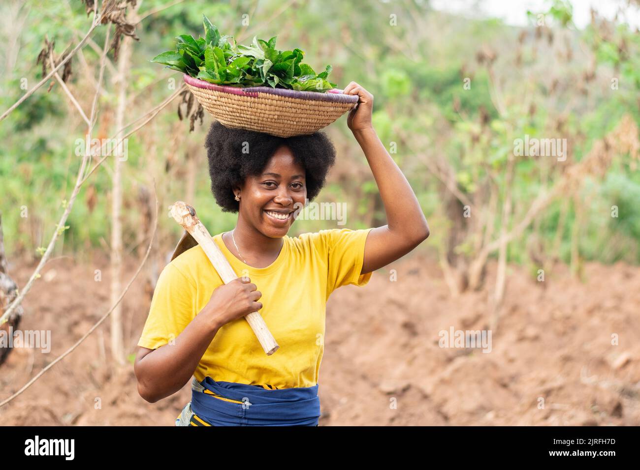 african farmer carrying vegetables and a hoe Stock Photo