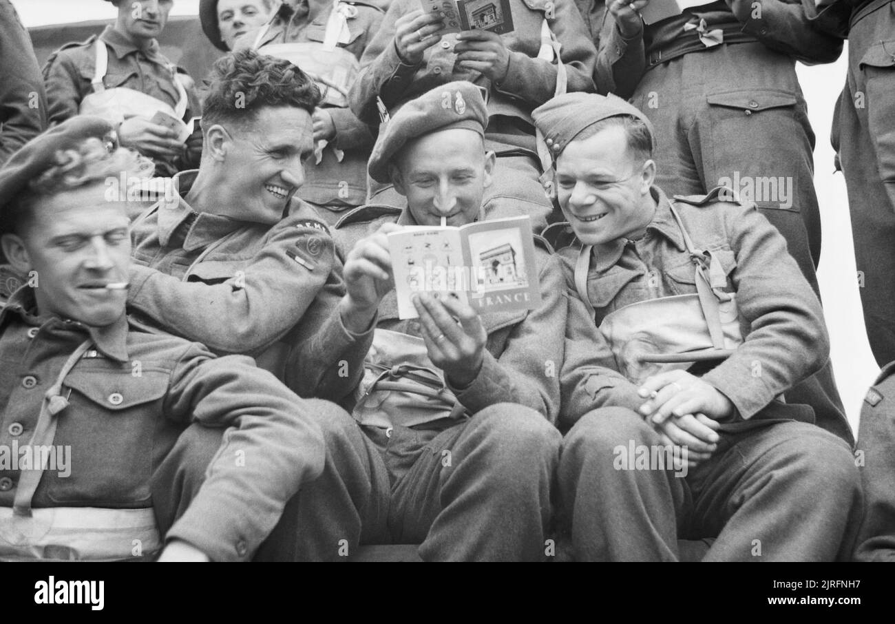 Operation Overlord (the Normandy Landings)- D-day 6 June 1944 The Final Embarkation: Three British soldiers of 51st Highland Division, aboard a landing craft, pass the time by reading the booklet on France which they were issued before embarkation. Stock Photo