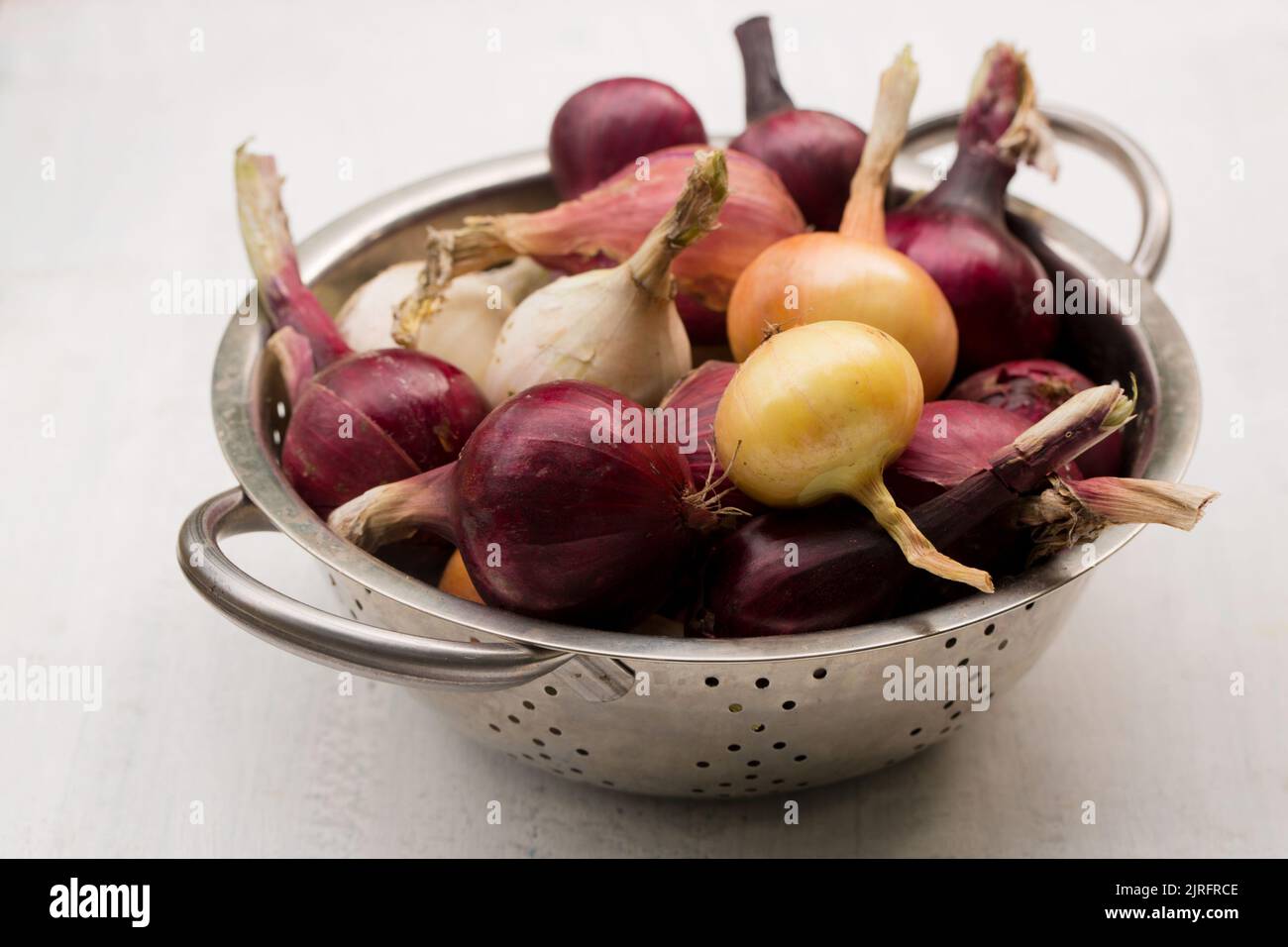 Purple, white and golden onions in a metal sieve on a light background Stock Photo