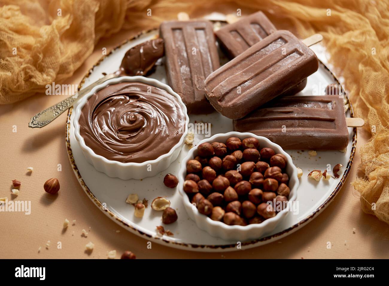 Chocolate popsicles with hazelnuts served with melted chocolate on a white plate Stock Photo