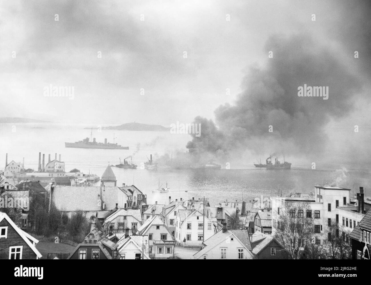 The Royal Navy during the Second World War British destroyers towing a captured petrol tanker, set ablaze by a German air raid, out into a Norwegian fjord to sink it in case of damage to other shipping. Part of the nearby town can be seen in the foreground. Stock Photo