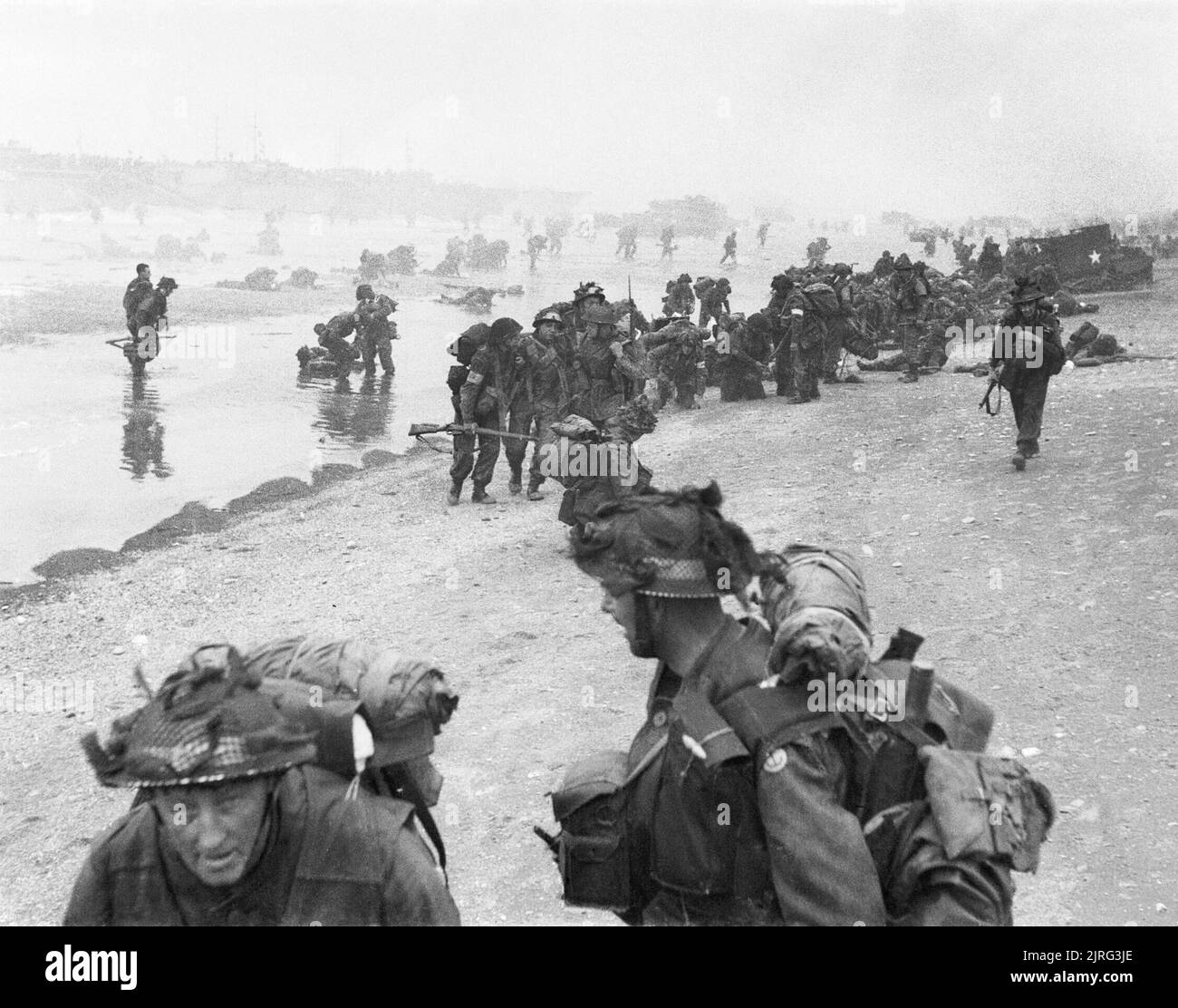 D-day - British Forces during the Invasion of Normandy 6 June 1944 Troops of 3rd Infantry Division on Queen Red beach, Sword area, circa 0845 hrs, 6 June 1944. In the foreground are sappers of 84 Field Company Royal Engineers, part of No.5 Beach Group, identified by the white bands around their helmets. Behind them, medical orderlies of 8 Field Ambulance, RAMC, can be seen assisting wounded men. In the background commandos of 1st Special Service Brigade can be seen disembarking from their LCI(S) landing craft. Stock Photo