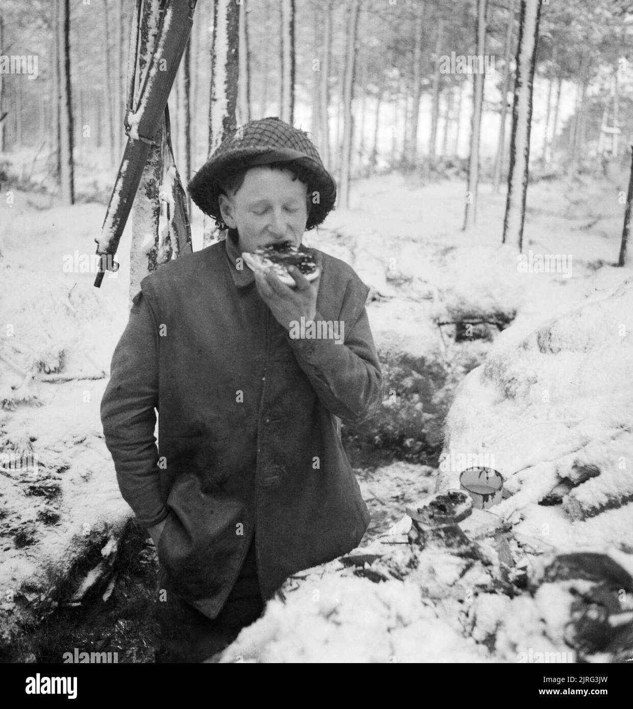 A British soldier eats his midday meal in a trench in the snow, while manning part of the front line along the River Maas in Holland, 8 January 1945. Private G Carnally eats his midday meal in a trench in the snow, while manning part of the front line along the River Maas in Holland, 8 January 1945. Stock Photo