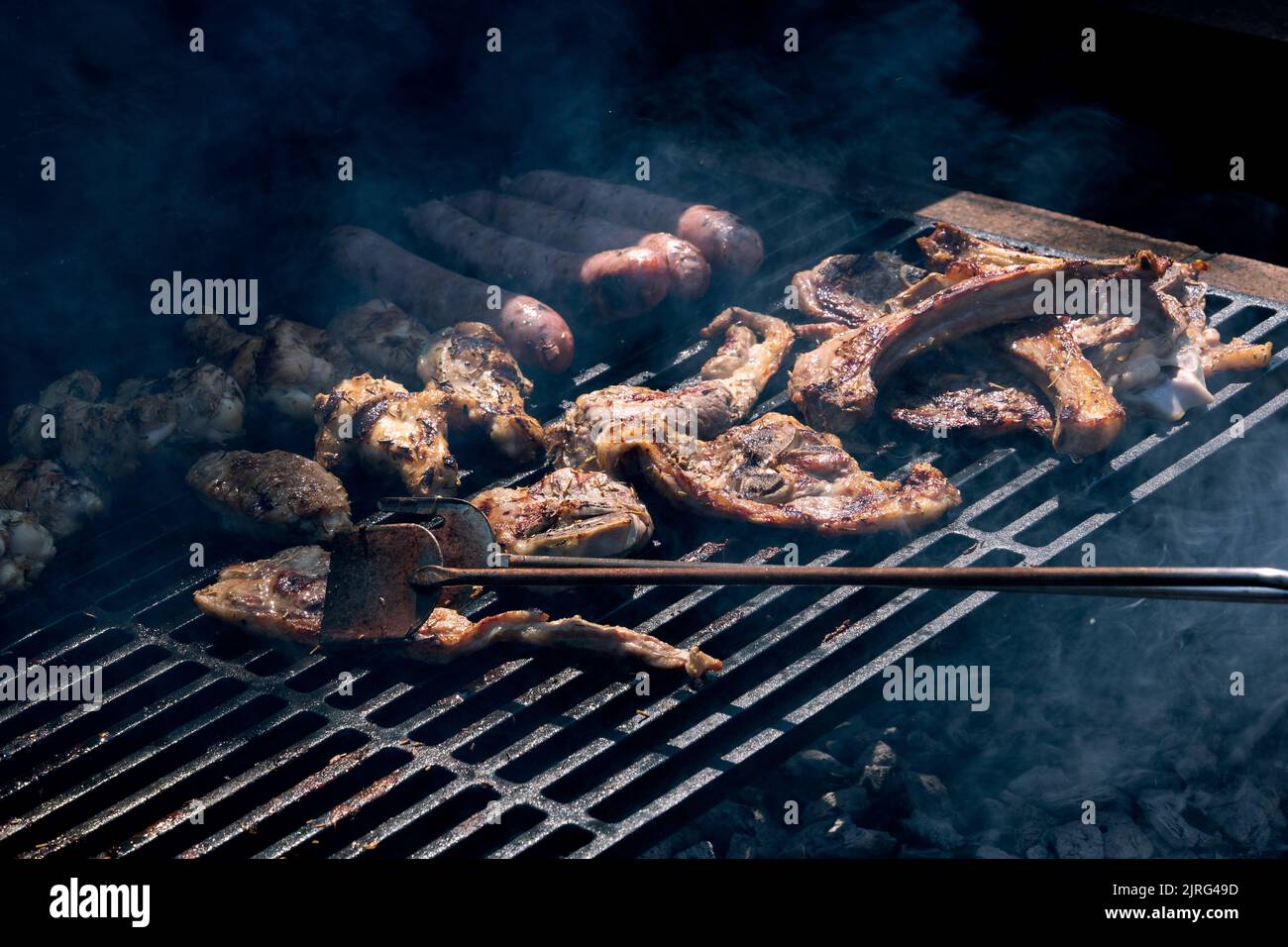 Grilled meat cooking on a wrought iron grill with the help of tongs