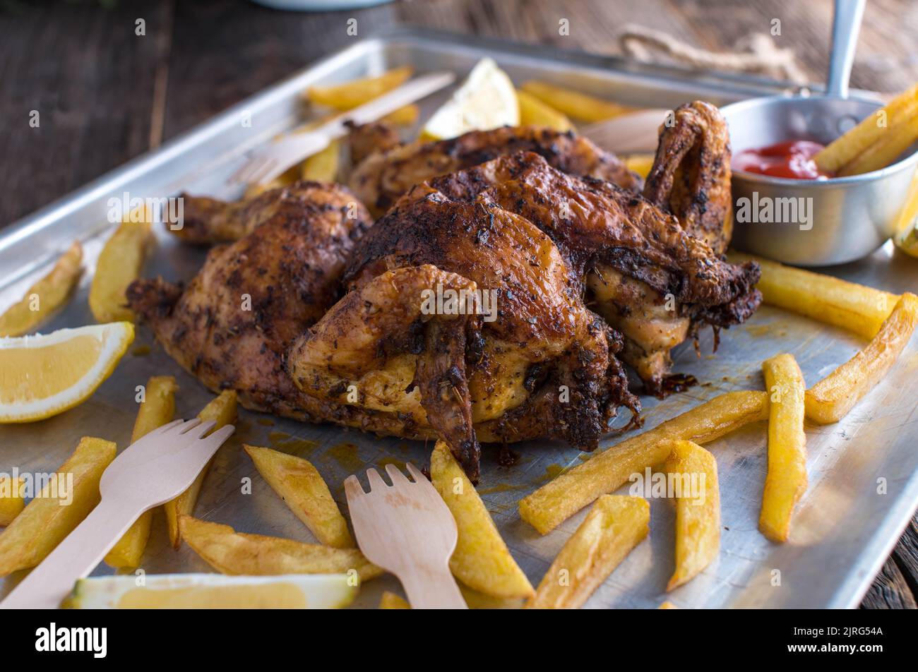 Crispy Spatchcock chicken with french fries on a baking tray Stock Photo