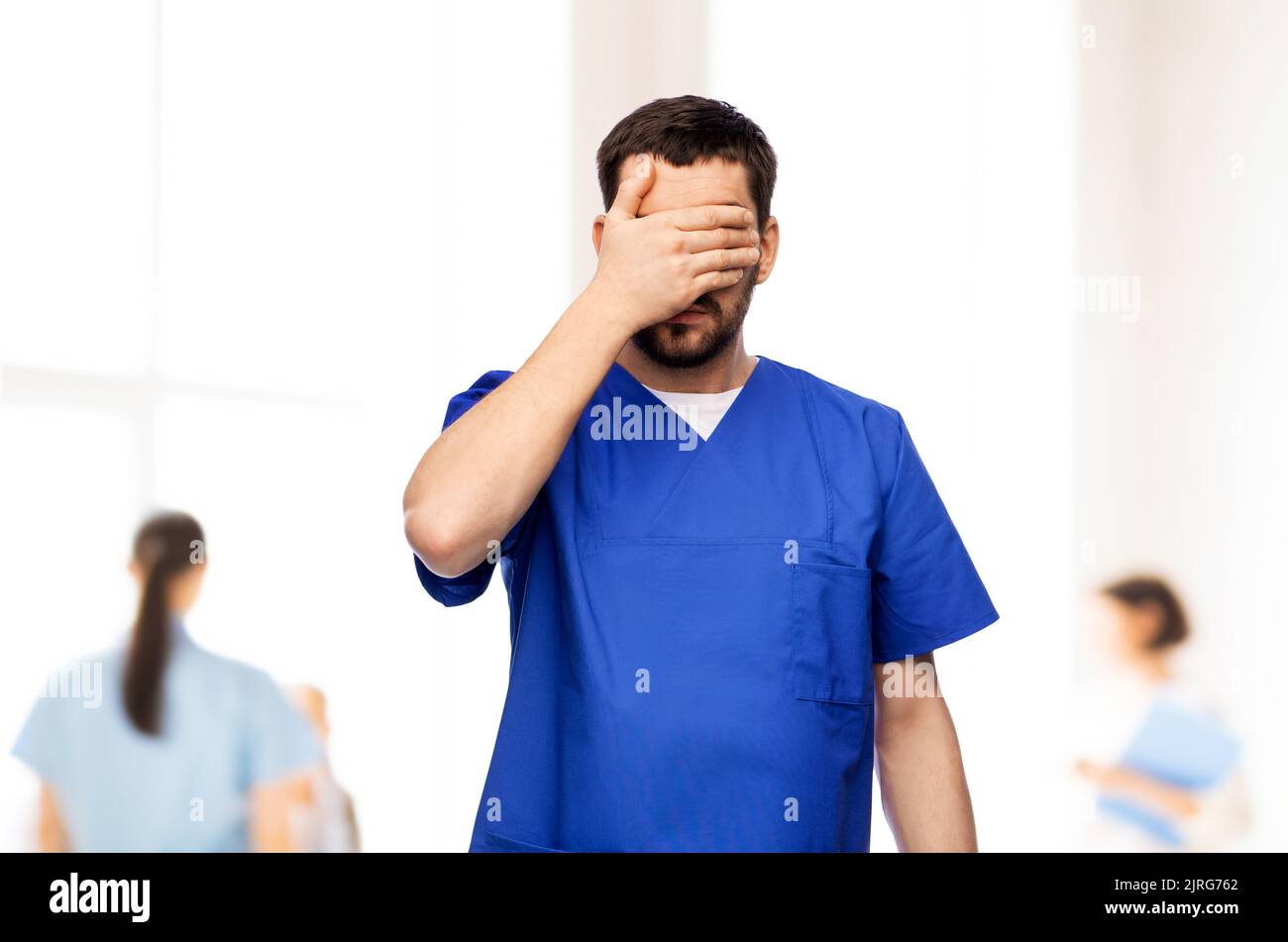 tired doctor or male nurse covering eyes with hand Stock Photo