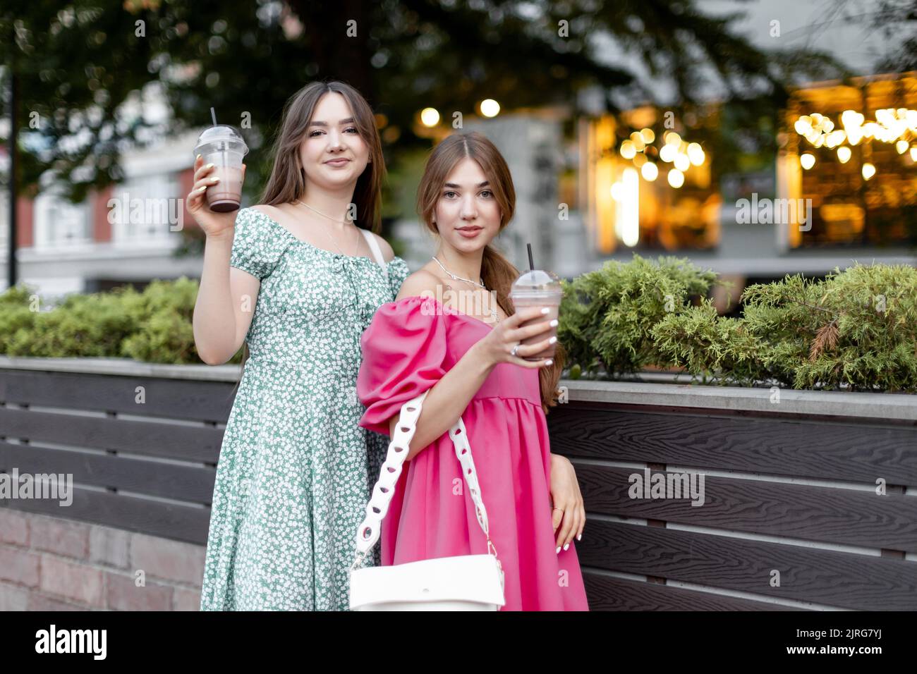 Two young beautiful smiling female in trendy summer clothes. Carefree women posing outdoors.Positive models holding and drinking cool drink in plastic Stock Photo