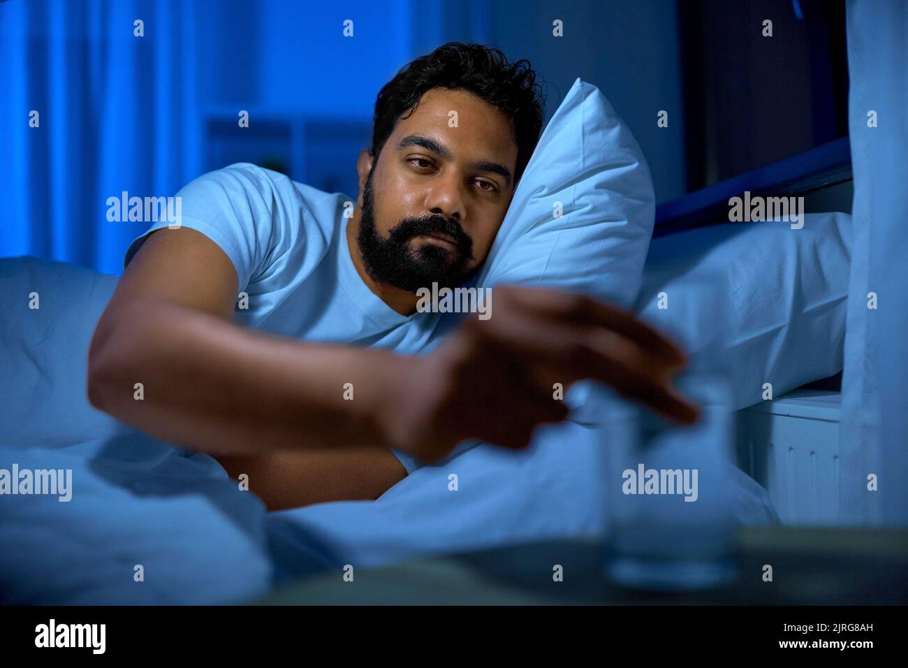 indian man drinking water in bed at night Stock Photo
