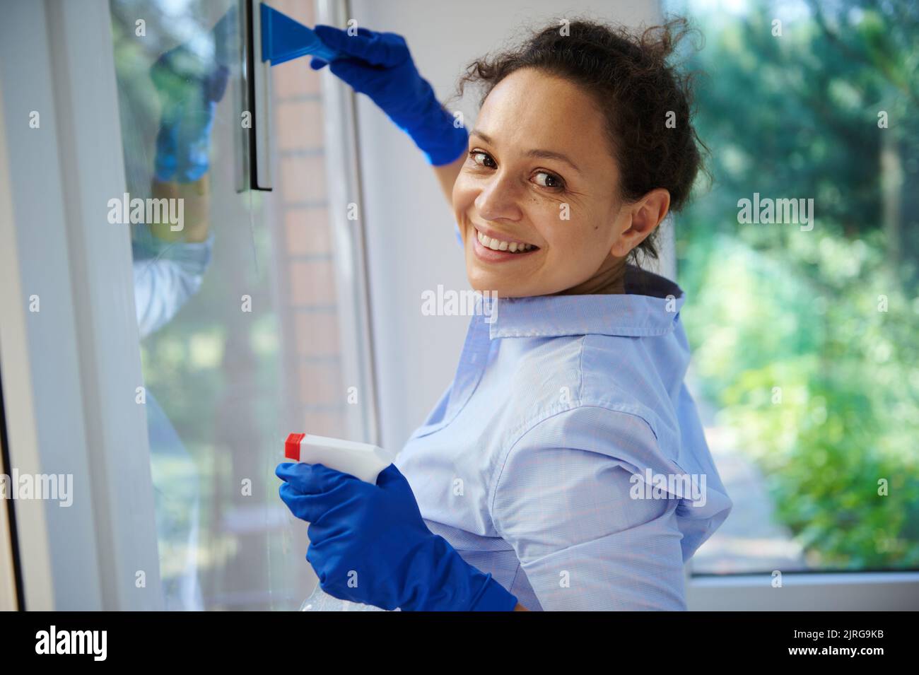 Multiethnic housewife washes and wipes window with detergent spray and