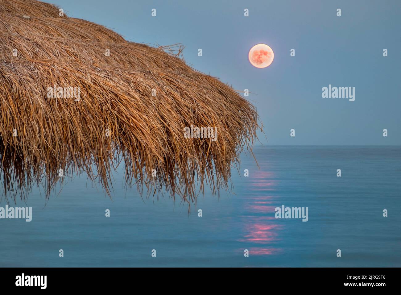 Seascape of the moonrise with an umbrella at the foreground made by straw in the beach of Agiokampos , Greece Stock Photo
