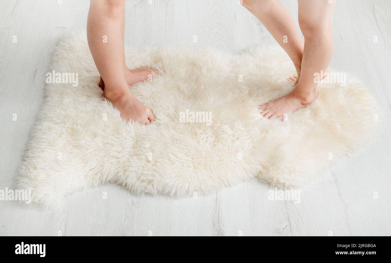 Close up view of 2 young girls sisters children standing with bare feet toes on very soft woolen sheepskin rug carpet. Cozy winter concept. Stock Photo