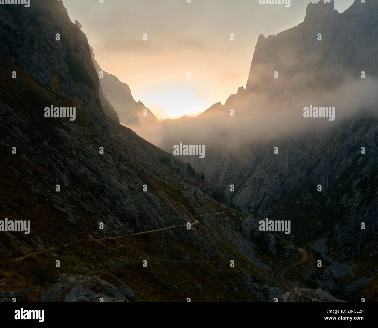 panorama of a mountain path through the interior of a canyon with the lights and mist of sunrise in the background Stock Photo