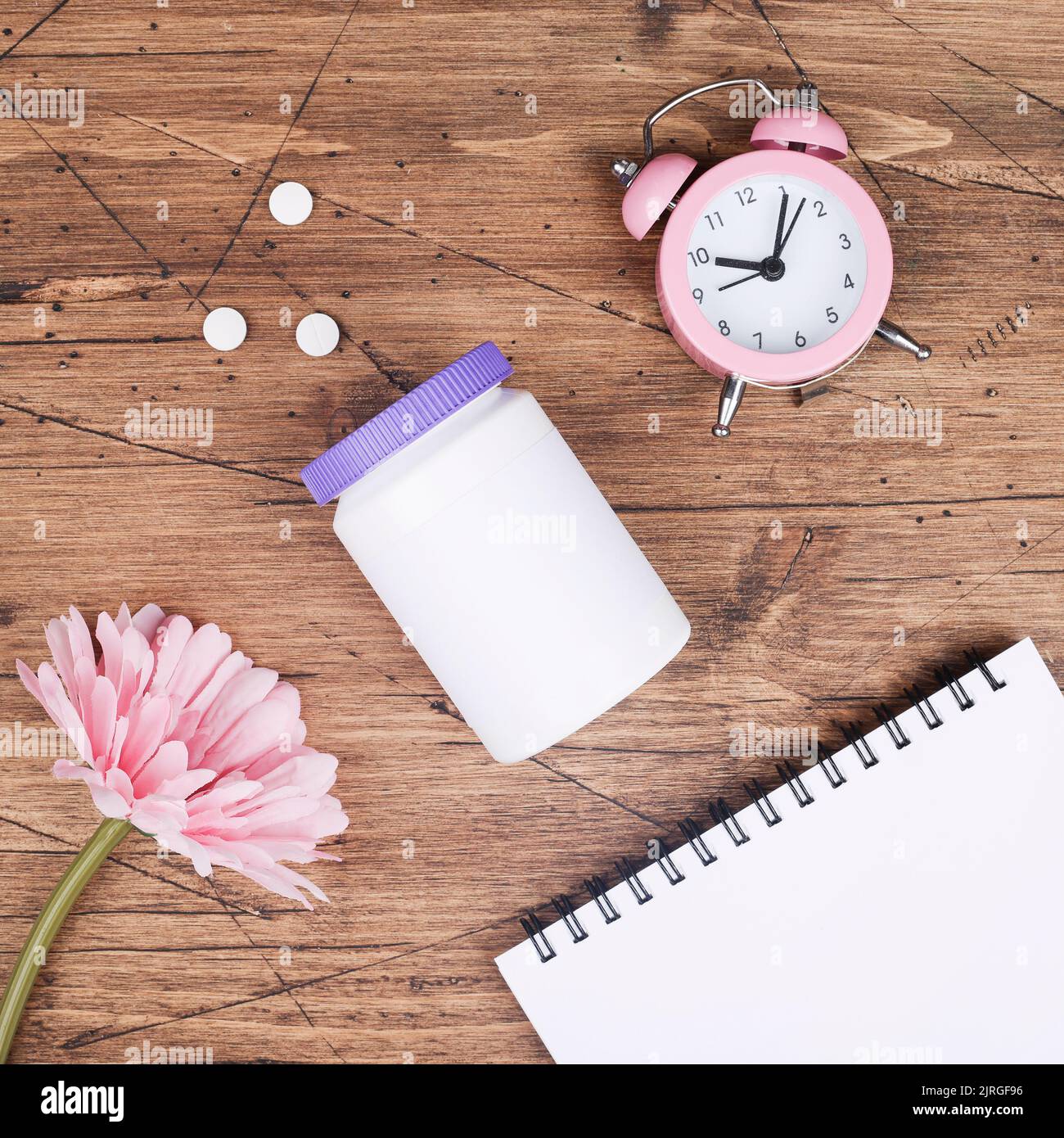 women health concept. medicine, health care style. copy space. white plastic bottle with pills, flowers, notebook and clock on wood background. square Stock Photo