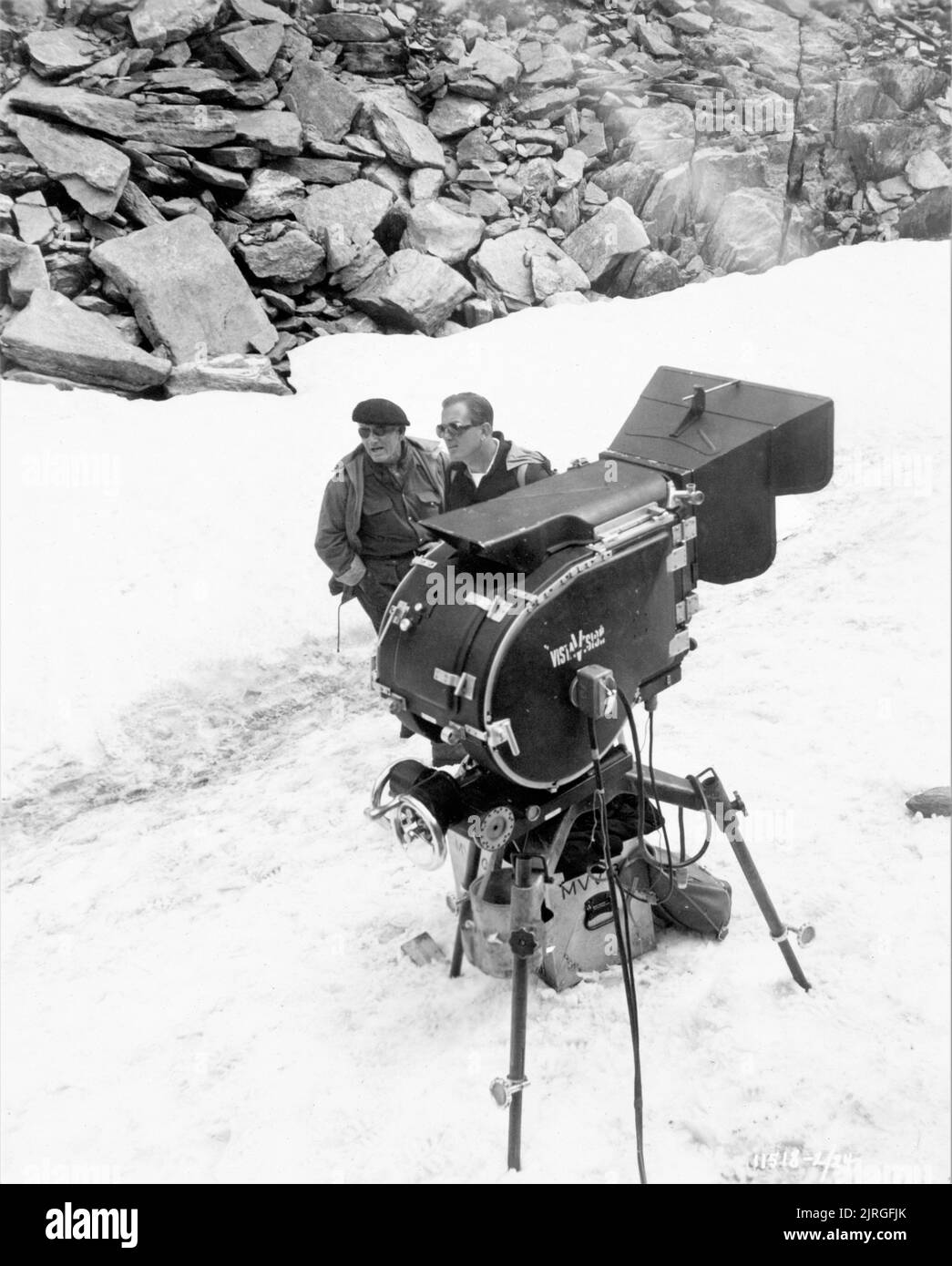 SPENCER TRACY and Director EDWARD DMYTRYK on set location candid in Mont Blanc area of France standing in snow next to VistaVision Movie Camera during filming of THE MOUNTAIN 1956 director / producer EDWARD DMYTRYK novel Henri Troyat Paramount Pictures Stock Photo