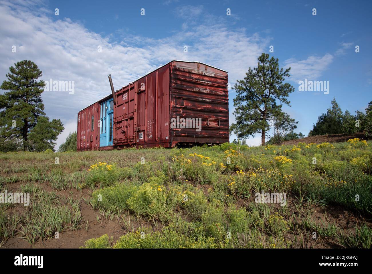 Dark red repurposed train car with turquoise blue doors in Northern New Mexico, Rio Arriba County, New Mexico, USA. Stock Photo