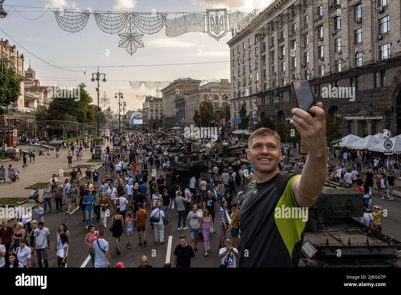 A man takes a selfie with a background of a crowd that has come to see the destroyed Russian military equipment in the exhibition on the streets of Kyiv. As dedicated to the upcoming Independence Day of Ukraine, and nearly 6 months after the full-scale invasion of Ukraine on February 24, the country's capital Kyiv holds an exhibition on the main street of Khreschaytk Street showing multiple destroyed military equipment, tanks and weapons from The Armed Forces of The Russian Federation (AFRF).As the Russian full invasion of Ukraine started on February 24, the war that has killed numerous civili Stock Photo