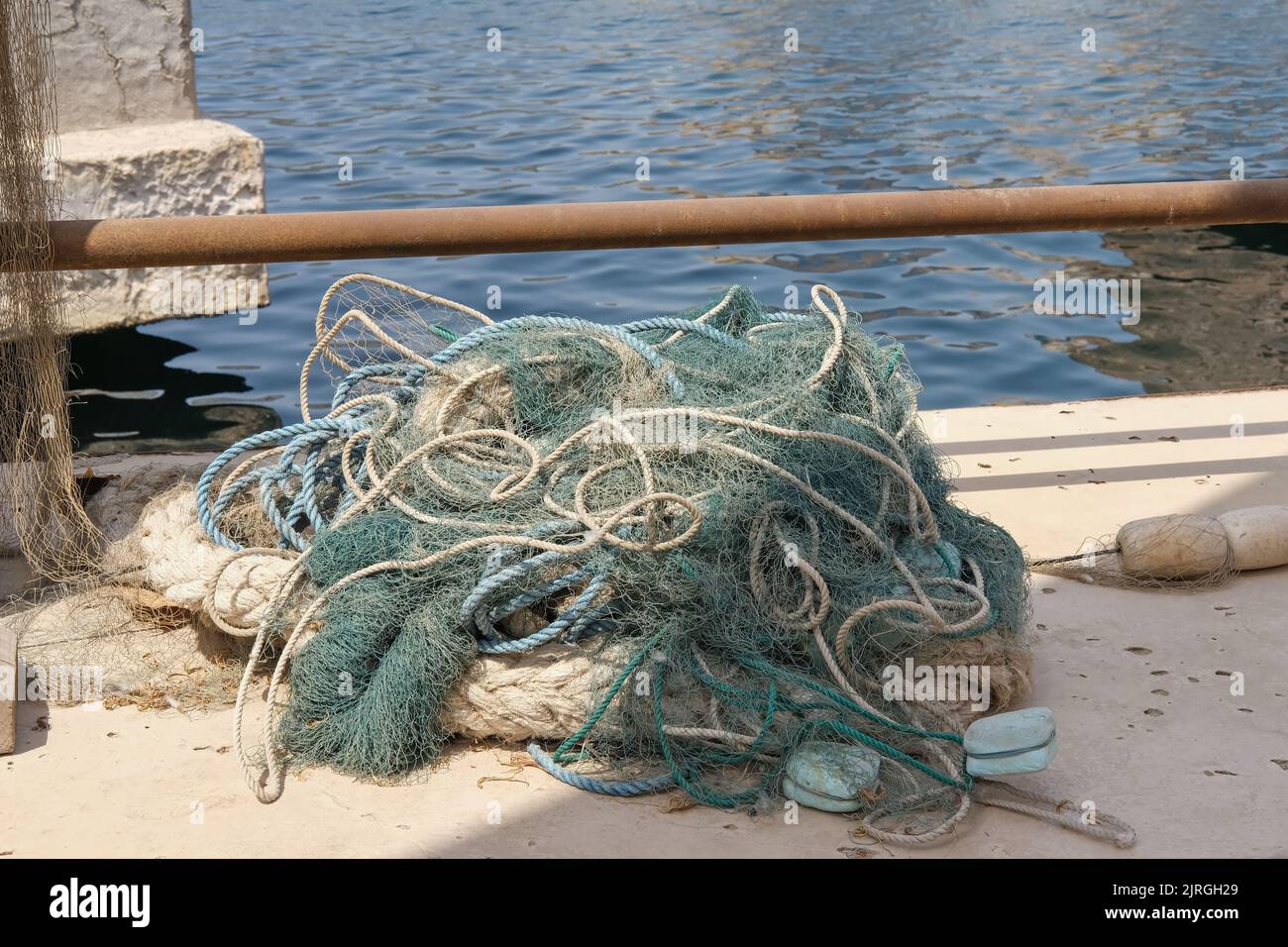 Braided fishing net from fibers woven in a grid-like structure with floats. Pile of fish mesh traps on the pier. Stock Photo