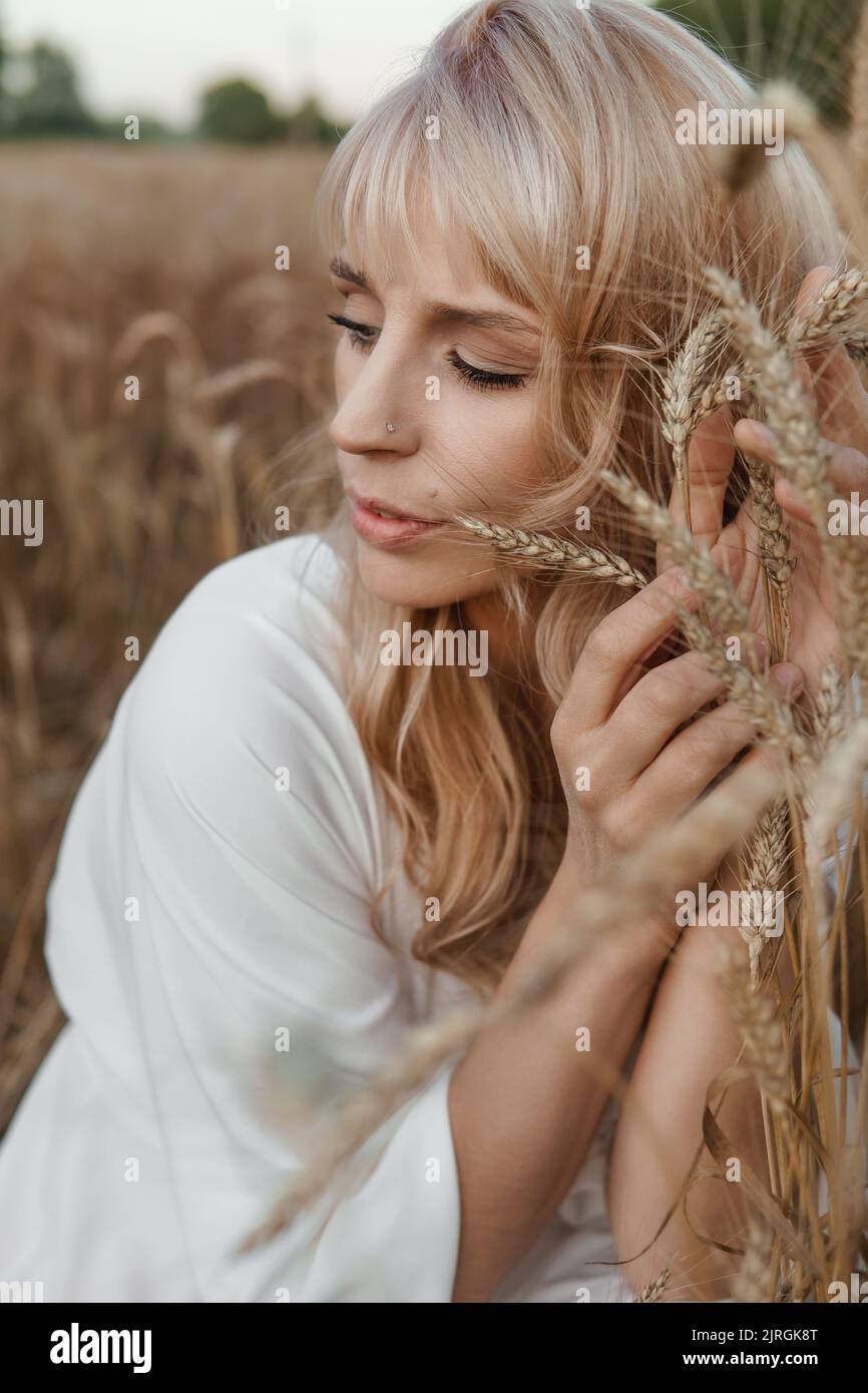 A blonde woman in a long white dress walks in a wheat field. The ...