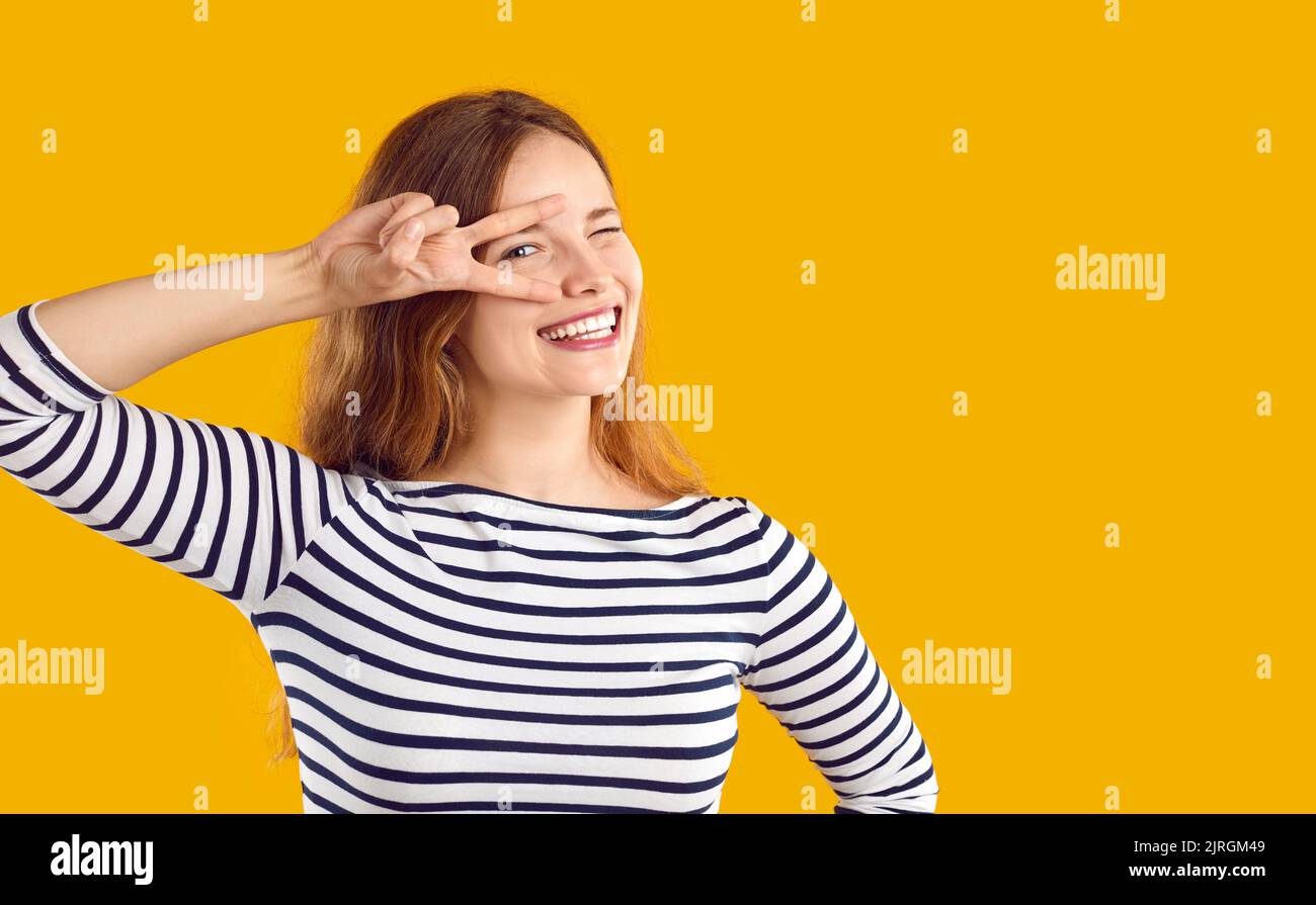 Happy young woman smiles, winks her eye and does peace, love and victory gesture Stock Photo