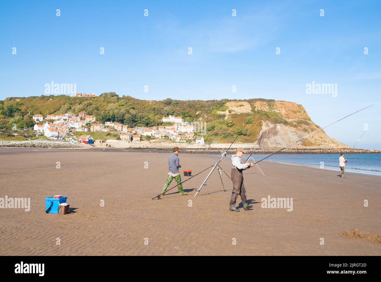 People fishing from Runswick bay beach with village in background. North Yorkshire, England, UK Stock Photo